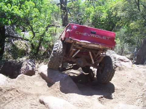 2004 Aston Martin Virage - This red Chevrolet pickup truck is shown from the rear as it maneuvers over large rocks on a dirt trail.
