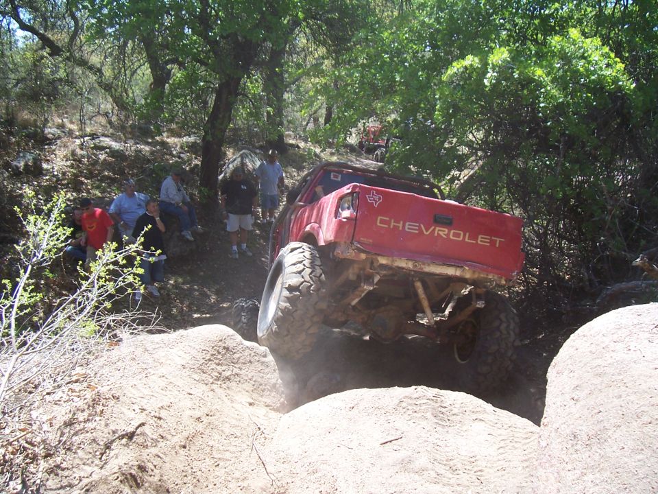 Red Chevrolet pickup truck with large tires navigating a sandy, rocky incline