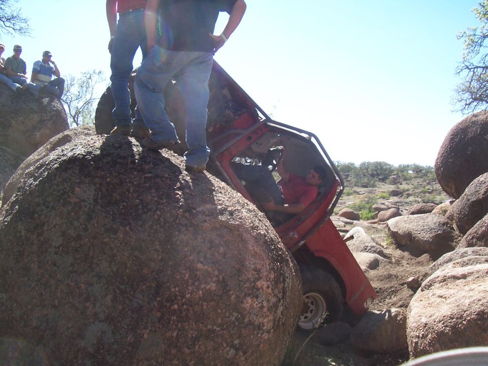 Red off-road vehicle wedged between large rocks, driver visible inside