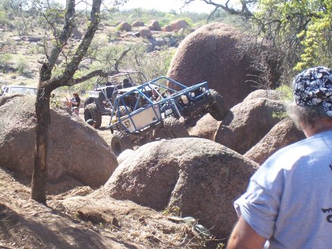 2004 Aston Martin Virage - Two off-road buggies navigate a rocky terrain, with one vehicle prominently featured as it climbs over large boulders.