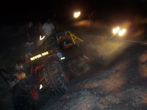 2004 Aston Martin Virage - Off-road vehicle with custom decals and roll cage navigates rocky terrain at night.