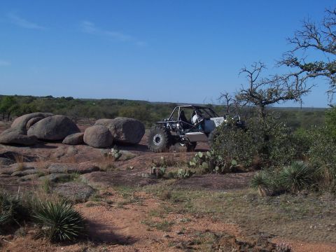 2004 Aston Martin Virage - A custom-built off-road buggy navigates a rocky landscape with sparse vegetation.