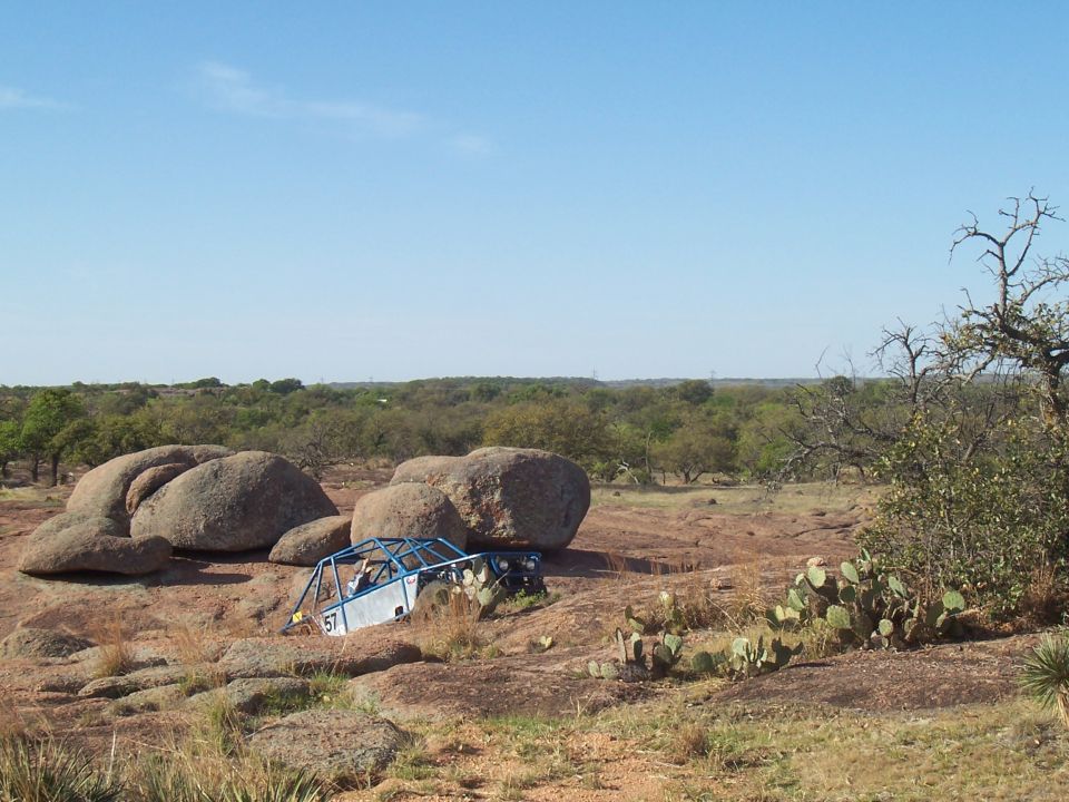 Buggy with a roll cage is stuck on rocks. Number 57 is visible on the side