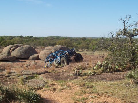 2004 Aston Martin Virage - A blue off-road buggy navigates a challenging rocky landscape under a clear blue sky.