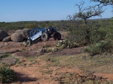 2004 Aston Martin Virage - A custom blue off-road buggy navigates a challenging rocky incline under a clear blue sky.