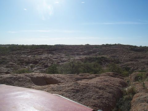 2004 Aston Martin Virage - The sun shines brightly on a desolate, rocky landscape, with the edge of a vehicle visible in the foreground.