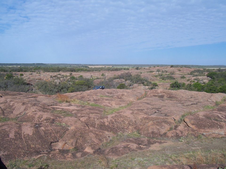 Dark SUV parked on a large expanse of pinkish-brown granite boulders under a partly cloudy sky