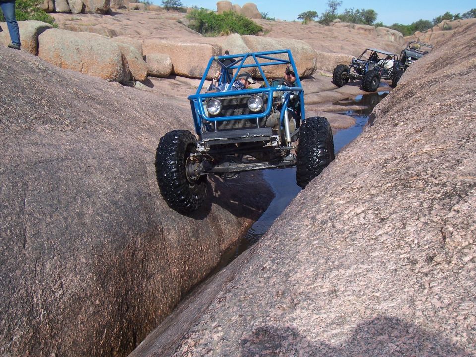 Blue tube-frame rock crawler buggy climbing over large boulders
