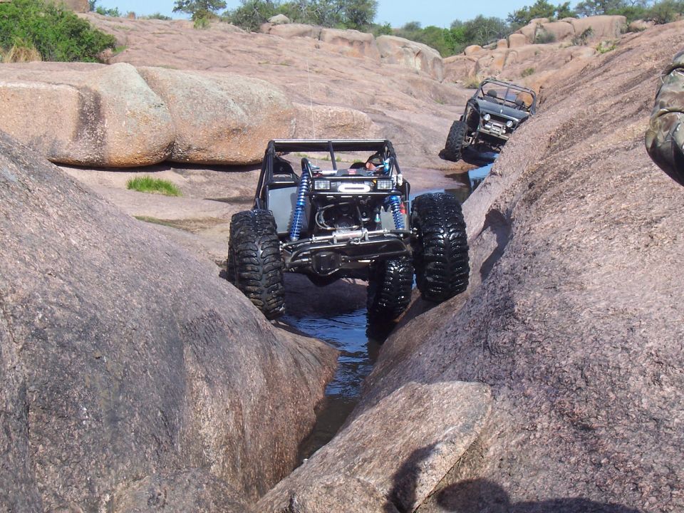 Black tube-chassis rock buggy in a granite gully with another vehicle behind