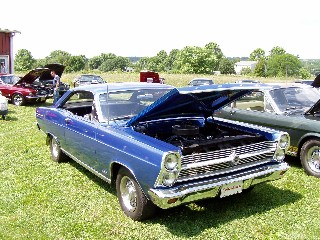 1999 Ford Crown Victoria - A blue 1966 Ford Fairlane 500 hardtop coupe is displayed with its hood open at a car show, alongside other vehicles.