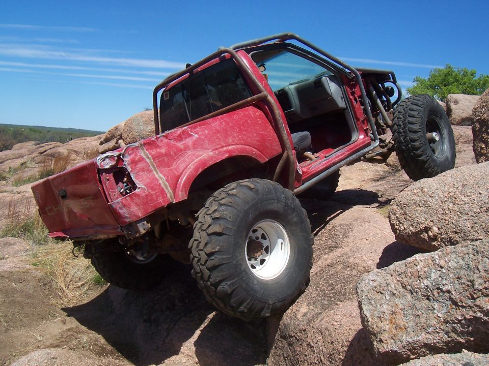 Rear view of red off-road truck climbing boulders