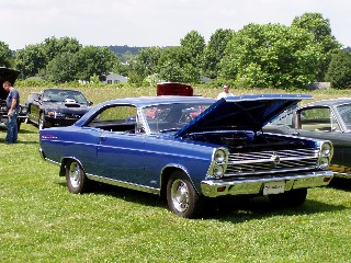 1999 Ford Crown Victoria - 1966 Ford Fairlane 500 coupe at a car show, hood open, with other vehicles visible.