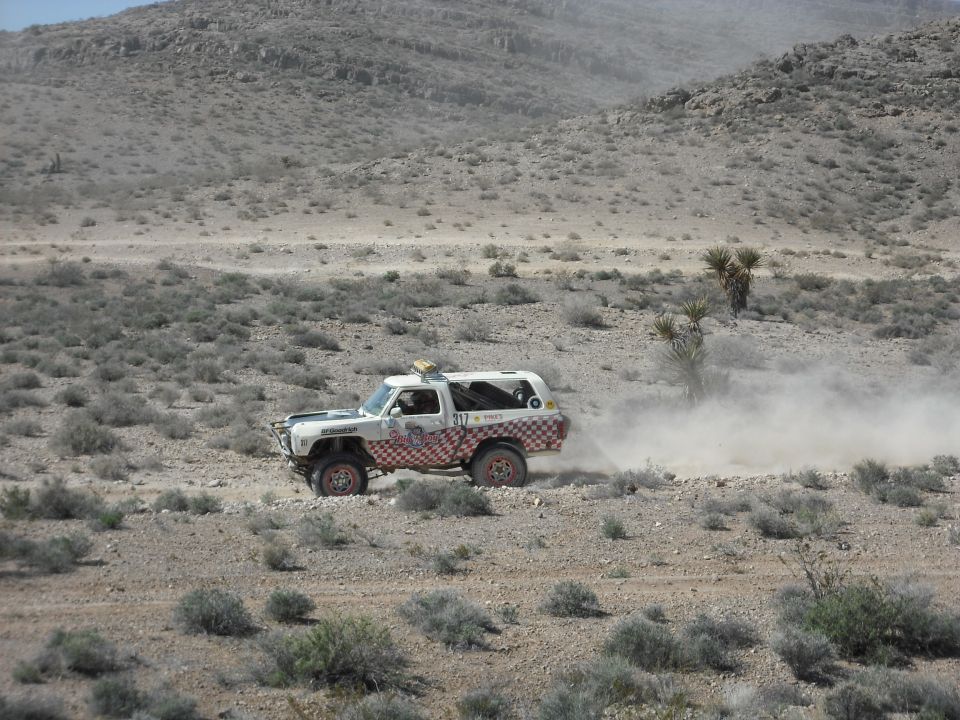 White and red off-road SUV racing through a dusty desert.