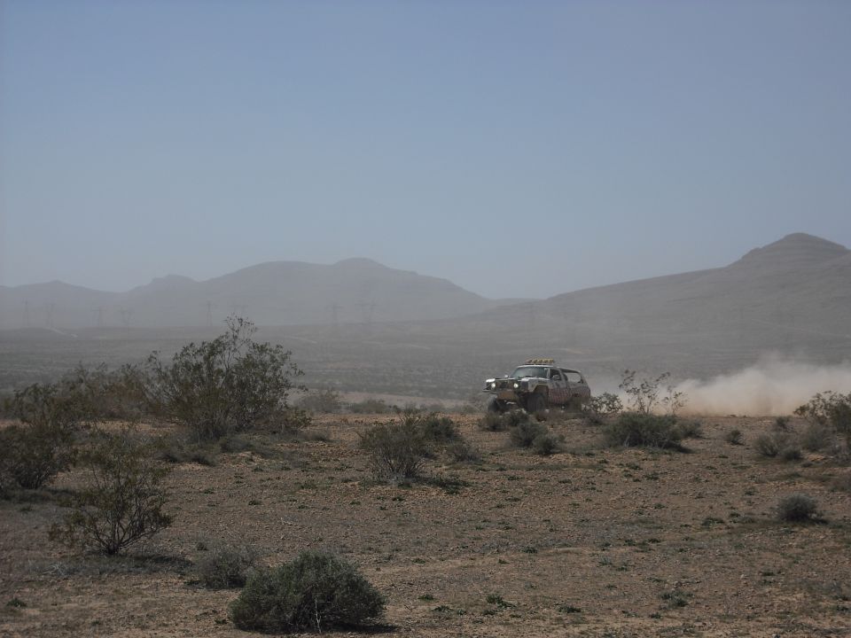 Off-road SUV racing through a dusty desert with mountains.