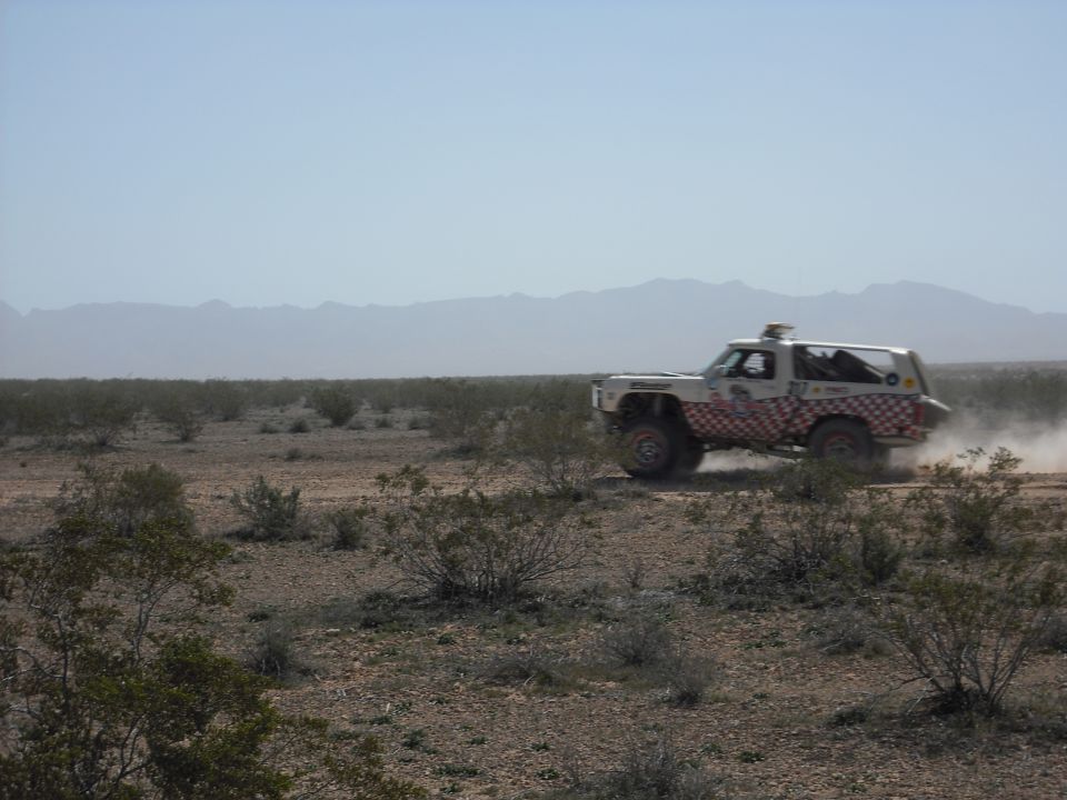 White off-road SUV with checkered graphics driving through a dusty desert landscape.