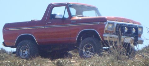 1986 Ford Bronco - A red Ford Bronco is parked on a dusty, overgrown hillside under a clear blue sky. The vehicle is viewed from a 3/4 front angle, showing it…