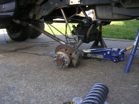 1996 Ford Bronco - The undercarriage of a vehicle is shown with the rear axle assembly partially removed, supported by a jack and jack stands. A new coil spri…