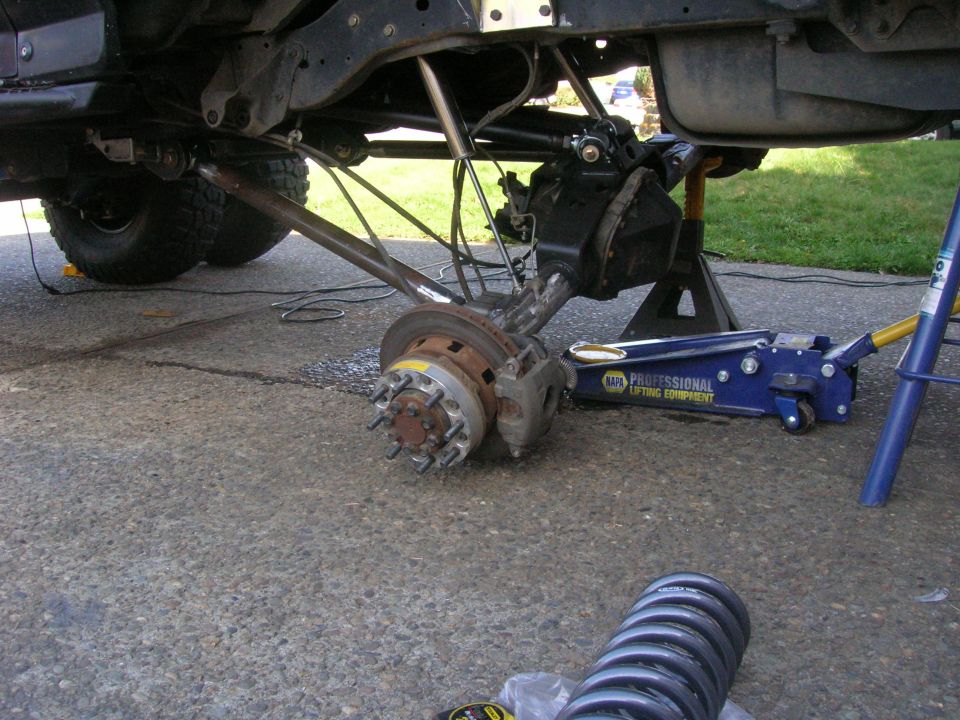 Undercarriage of a vehicle with rear axle assembly removed, jack, jack stands, and new coil spring.