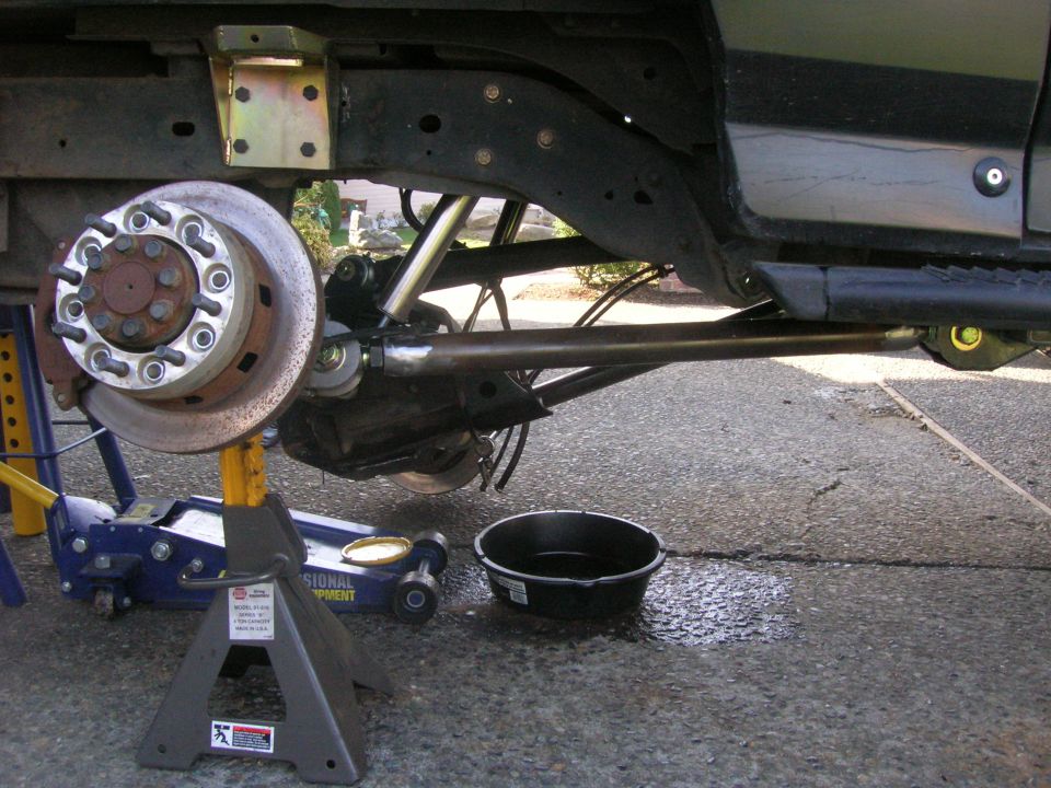 Undercarriage of a lifted 1996 Ford Bronco with front wheel, brake rotor, suspension, jack, and jack stands.