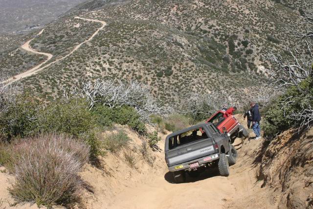 Two off-road trucks on a steep mountain trail.