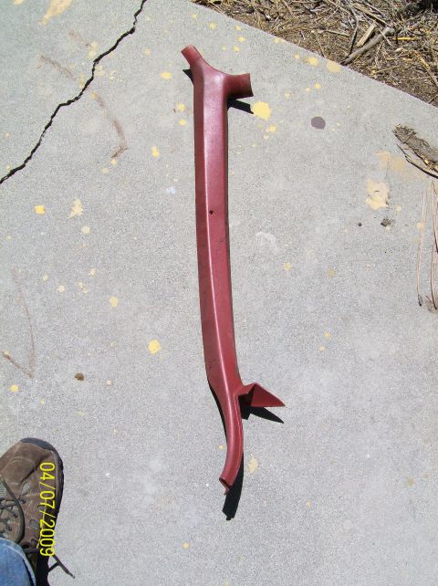 1972 Ford Ranchero - A red plastic trim piece, possibly for a car's interior pillar, lies on a concrete surface with some debris and a shoe in the lower left co…
