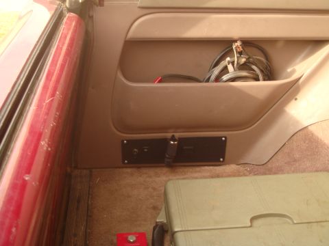 1992 Ford Bronco - The interior of a vehicle shows a storage pocket with jumper cables and a black panel with a 12v power outlet and a switch.