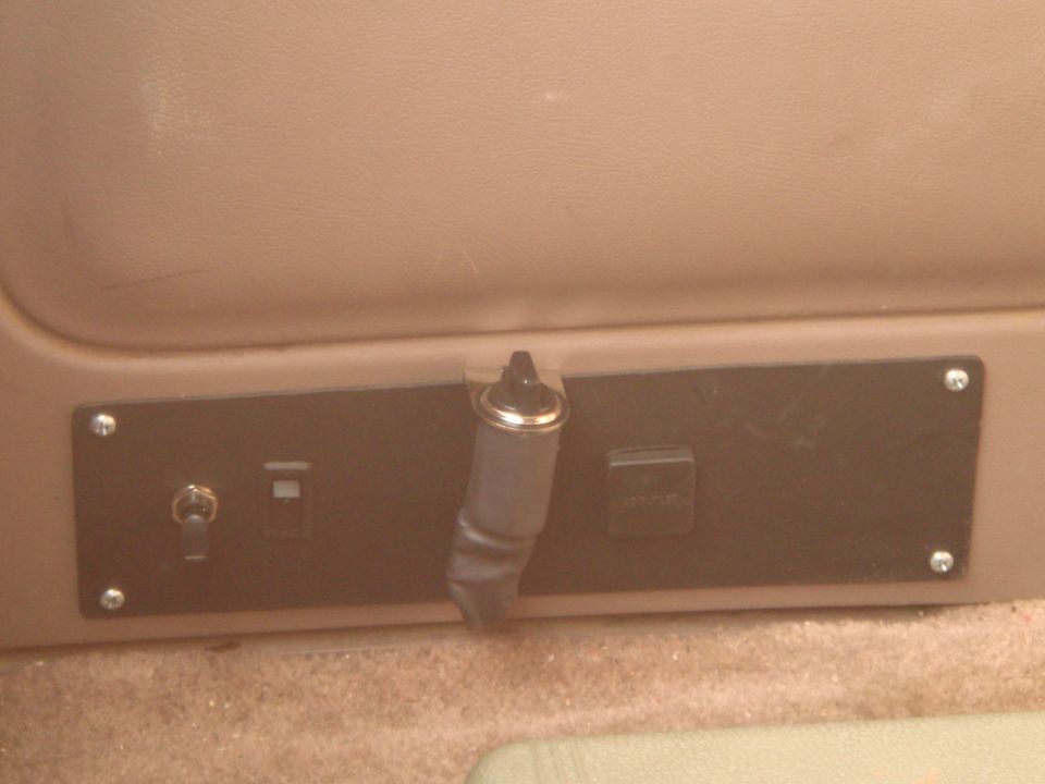 Close-up of a 12V outlet and toggle switch on a black panel.