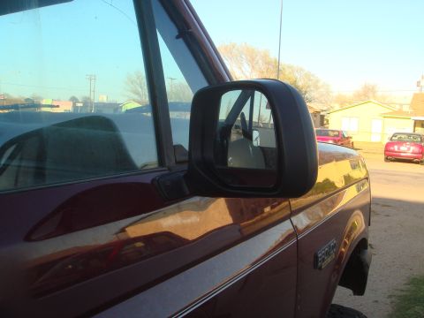1992 Ford Bronco - The side view mirror and portion of the driver's side door of a maroon SUV are visible. The reflection in the mirror shows the interior of…