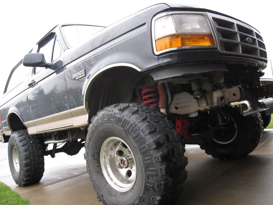 Lifted black 1996 Ford Bronco with large off-road tires, close-up low angle.