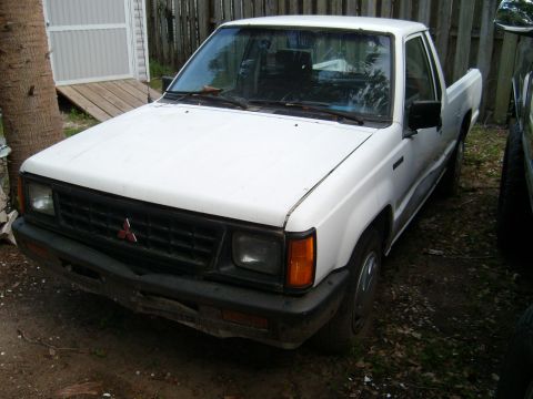 1992 Ford Bronco - The front 3/4 view of a white, older model pickup truck is shown parked on a dirt lot with some vegetation. The truck has a black grille wi…