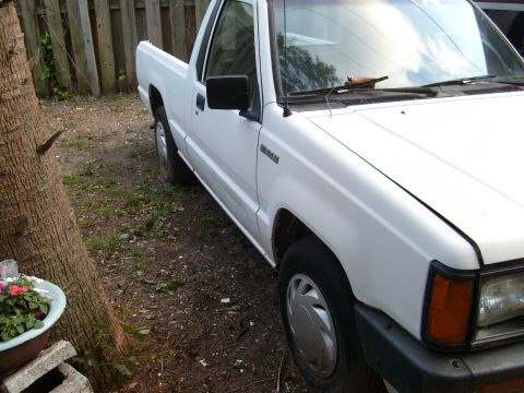 1992 Ford Bronco - The right side of a white pickup truck is shown parked on a dirt lot next to a wooden fence. The front passenger side wheel and fender are…