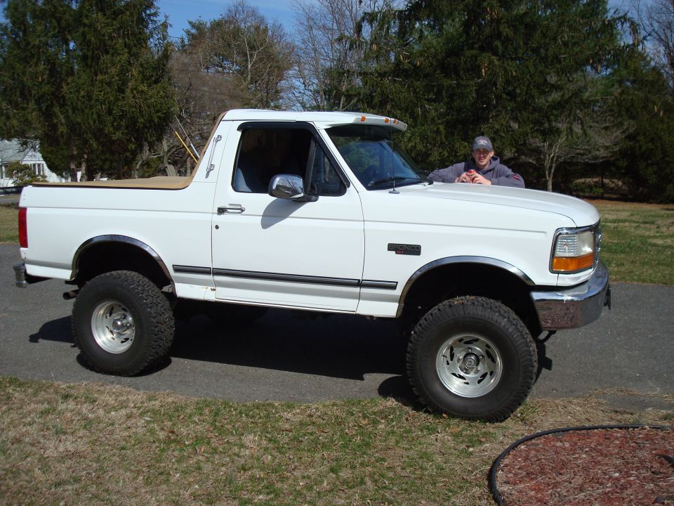 White Ford Bronco with a person leaning on the hood