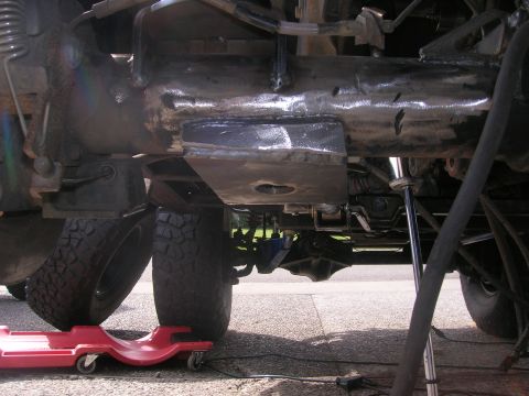 1996 Ford Bronco - This is a close-up underside view of a heavily modified vehicle frame, showing custom metal fabrication and welding work. The vehicle's tir…