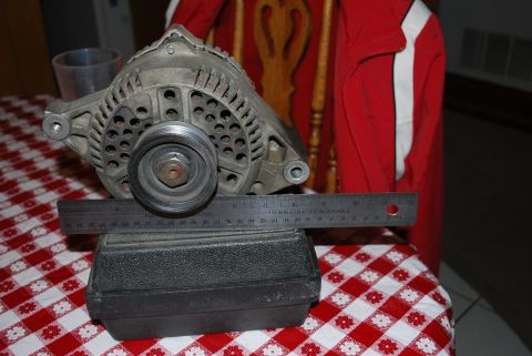 1996 Ford Bronco - An alternator is shown with a ruler placed across it to measure its dimensions.