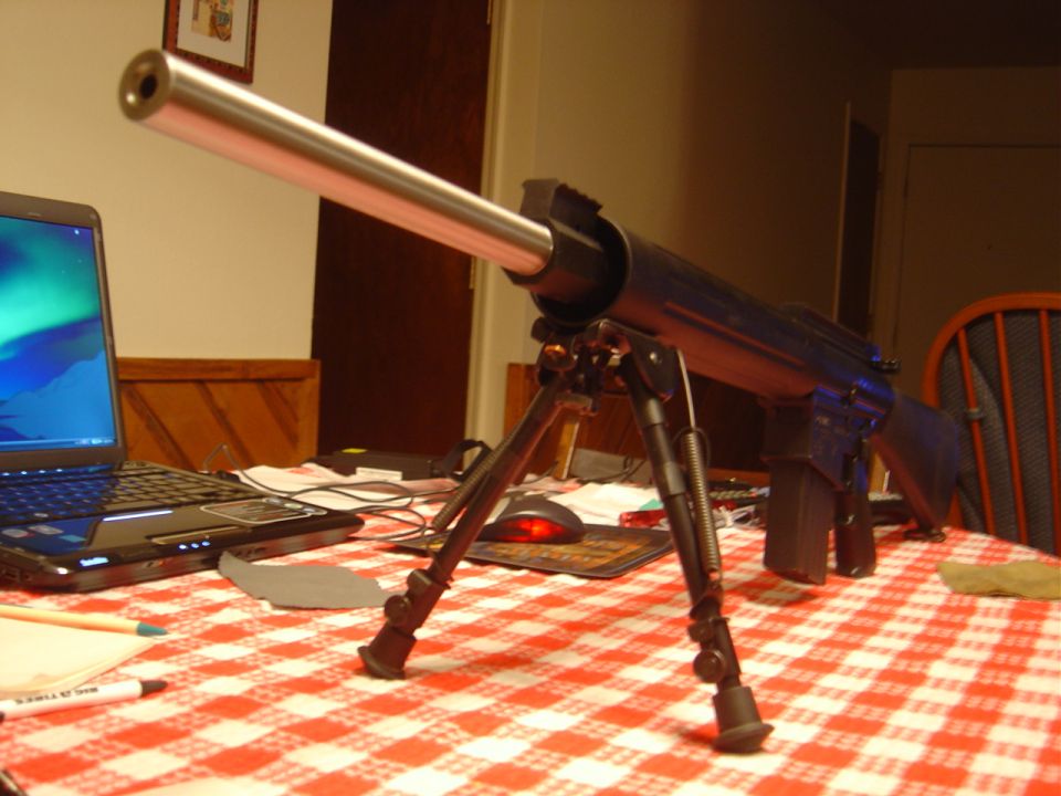 Rifle with bipod on a red and white checkered tablecloth, next to a laptop