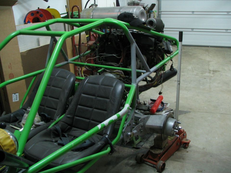 Green tube-frame buggy with bucket seats and engine in garage