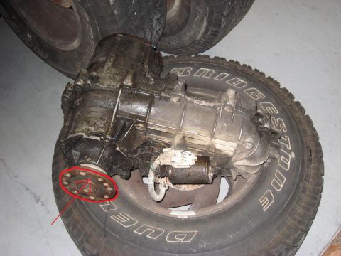 1991 Ford Bronco - A greasy transfer case sits on a tire, with a red circle pointing to its output flange.