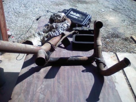 1992 Ford C-350 (Centurion Conversions) - Various exhaust pipe components and a turbocharger are laid out on a wooden surface, possibly for replacement or repair.