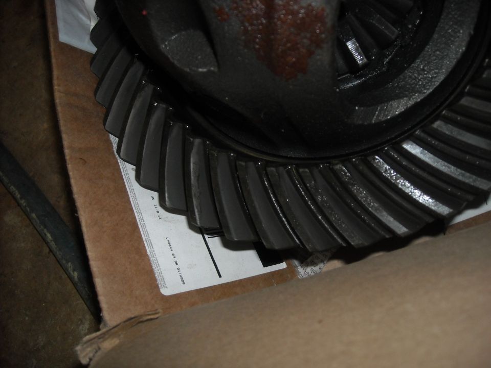 Close-up of a differential gear set with visible teeth. A shipping label is partially visible underneath