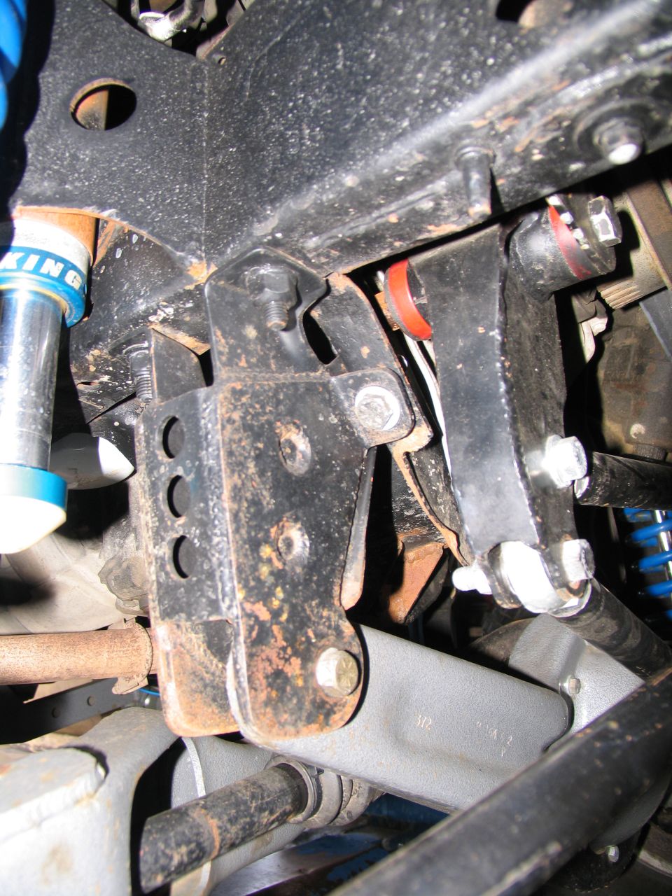 Close-up of rusty black metal suspension parts with blue shock absorber and red bushings