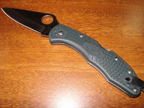 2000 Ford Crown Victoria - A close-up view of a green folding knife with a black blade is shown on a wooden table.