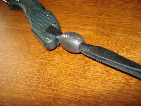 2000 Ford Crown Victoria - A close-up view of a knife handle attached to a black leather lanyard with a metal bead.