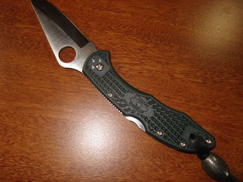 2000 Ford Crown Victoria - A close-up view of a green folding knife with a silver blade resting on a wooden surface.
