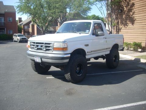1992 Ford Bronco - Lifted 1992 Ford Bronco with large tires is parked in a lot next to an apartment building.