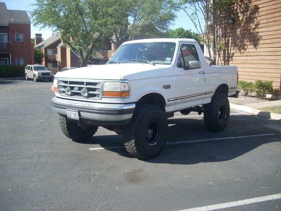Lifted white Ford Bronco with top removed, mud tires and steel wheels in a parking lot