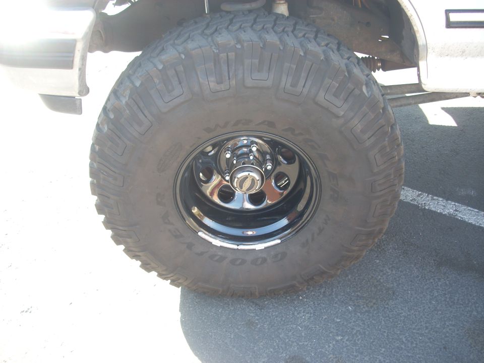 Close-up of a large off-road tire on a black rim with chrome lug nuts
