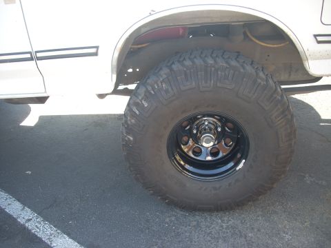 1992 Ford Bronco - Close-up of a white SUV's wheel and fender, showing a large tire and black steel rim.