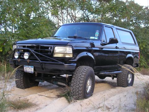 1995 Ford Bronco - This black Ford Bronco is shown with a custom front bumper and off-road tires, resting on a sandy surface.