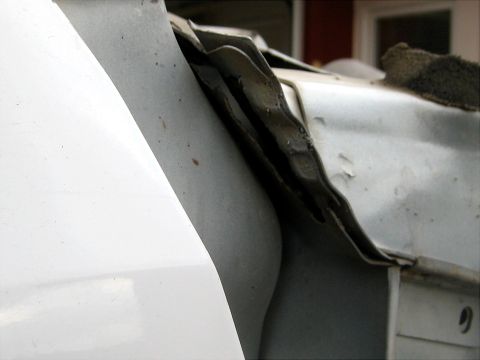 1996 Ford Bronco - Close-up of a buckled and split seam where a white fender meets the inner apron, the folded sheet metal wrinkled and torn open along the jo…
