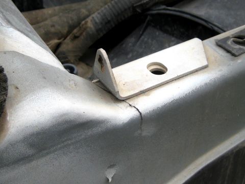 1996 Ford Bronco - Close-up of a factory L-shaped mounting tab with a single bolt hole on a vehicle's inner fender rail, with a visible crack running through…